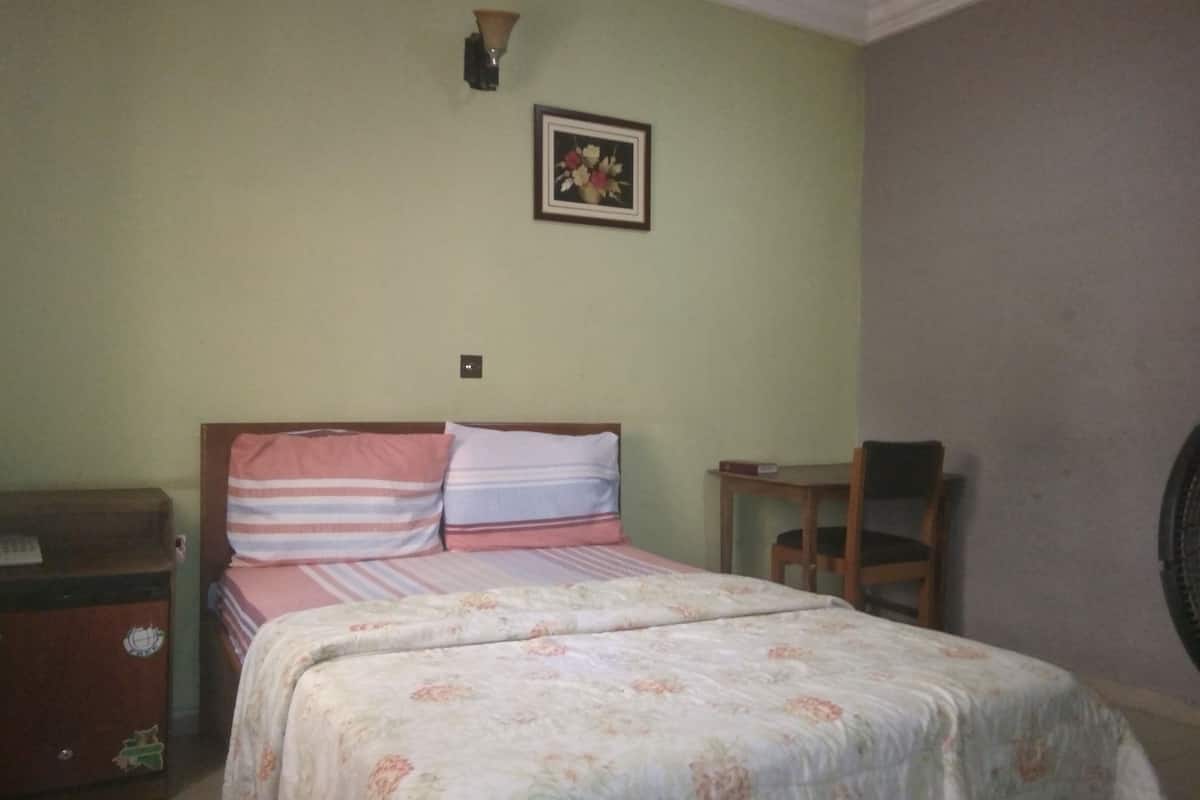 Un dormitorio con cama, mesita de noche, silla y lámpara de pared.