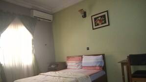 Un dormitori amb un llit, una taula de nit, una cadira, aire condicionat fixat a la paret i un quadre emmarcat a la paret.