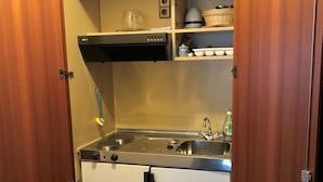 A compact kitchen with a stove, sink, and storage cabinets. - Cafe Best Gästezimmer (Erbach)