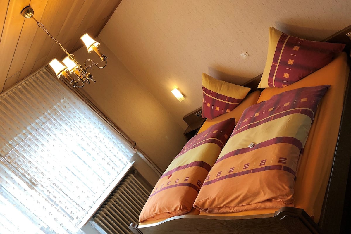 A bed with patterned pillows, a wooden headboard, and a wall-mounted light fixture.