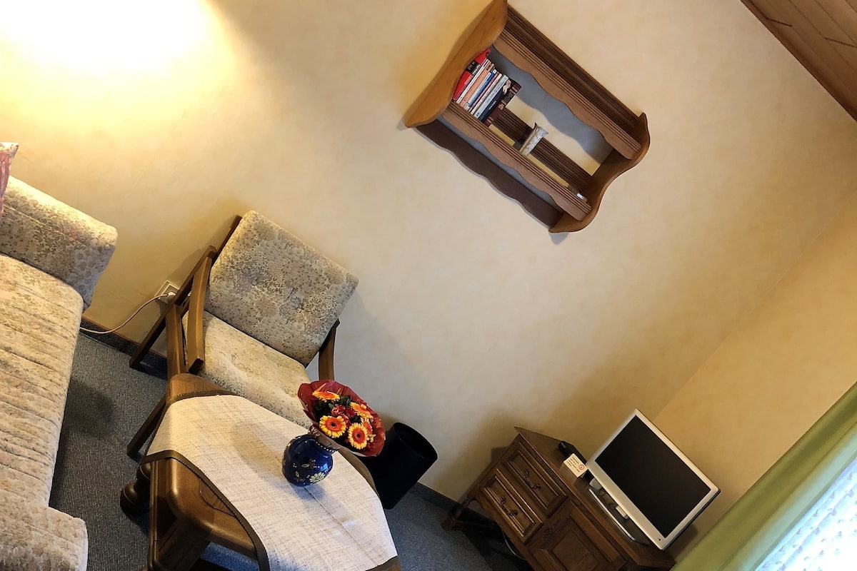 A cozy room with a sofa, a small wooden table, a bookshelf, and a radiator.