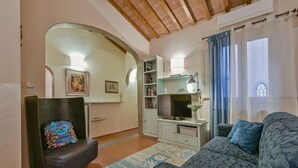Een woonkamer met een bank, een fauteuil, een televisie en een boekenkast.