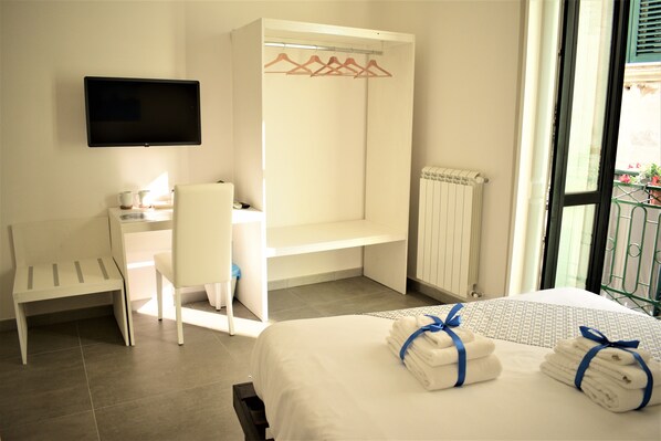 Une chambre d’hôtel équipée d’un lit, d’un bureau, d’une chaise, d’une télévision et d’une fenêtre donnant sur l’extérieur.