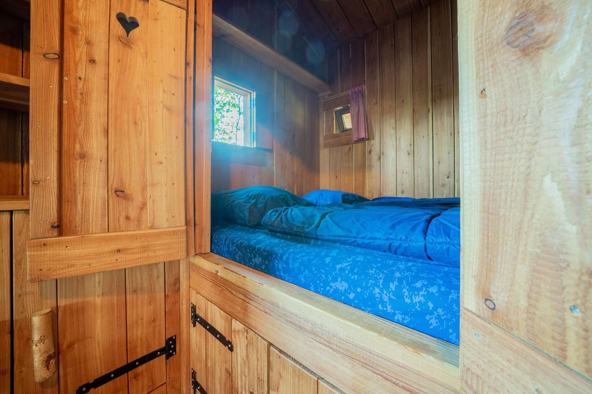 Une pièce dans un chalet en bois, comprenant un lit, une fenêtre et un petit placard.