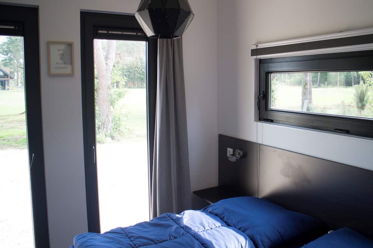 Une chambre à coucher avec un lit, une fenêtre, une porte et un luminaire fixé au mur.