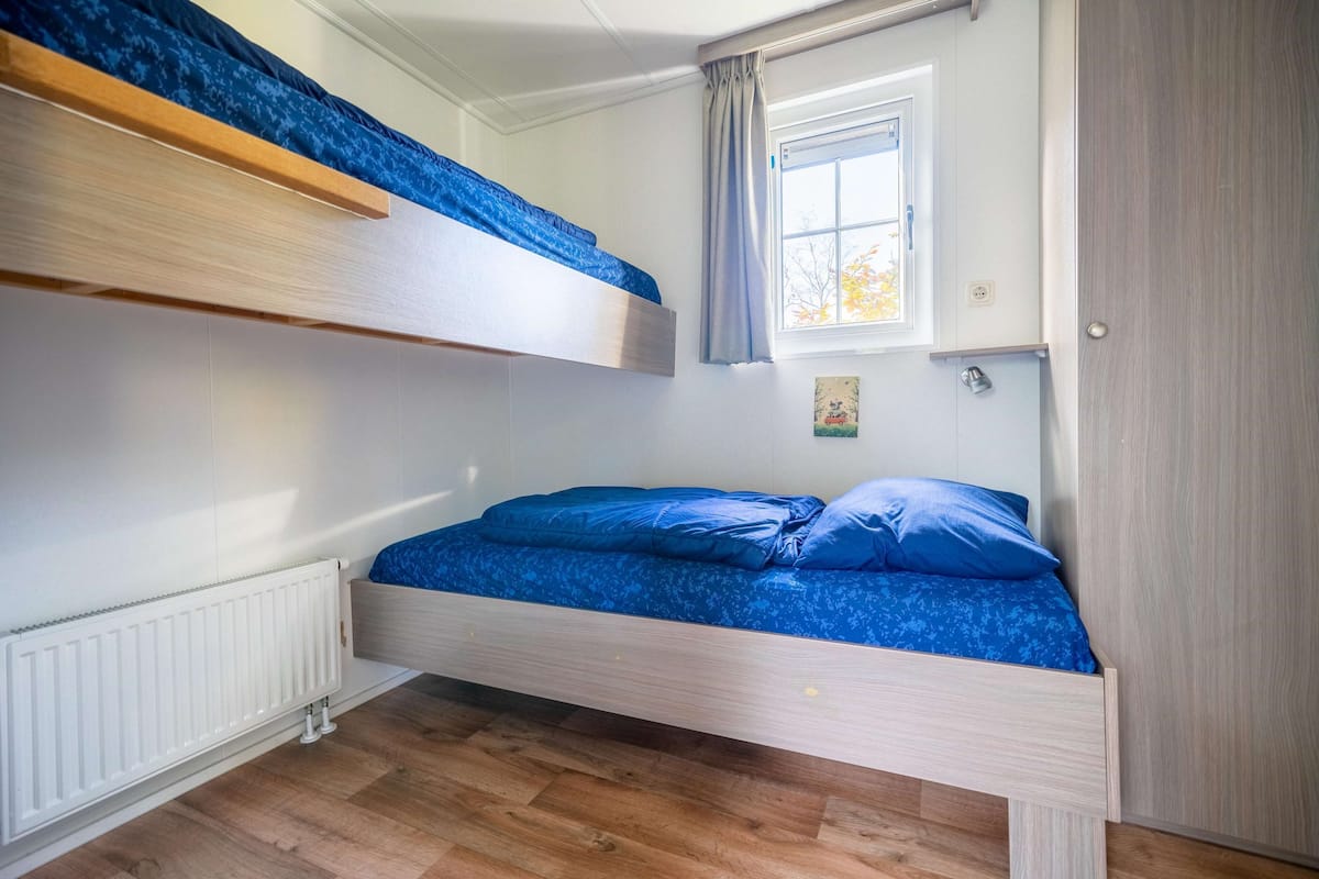 Une chambre avec un lit superposé, une fenêtre, un radiateur et une porte.