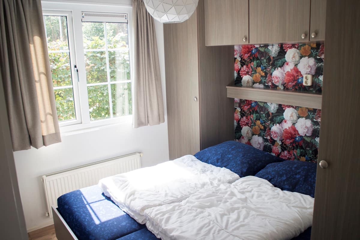 Une chambre à coucher avec un lit, une fenêtre avec des rideaux, un radiateur et un papier peint à motifs floraux.