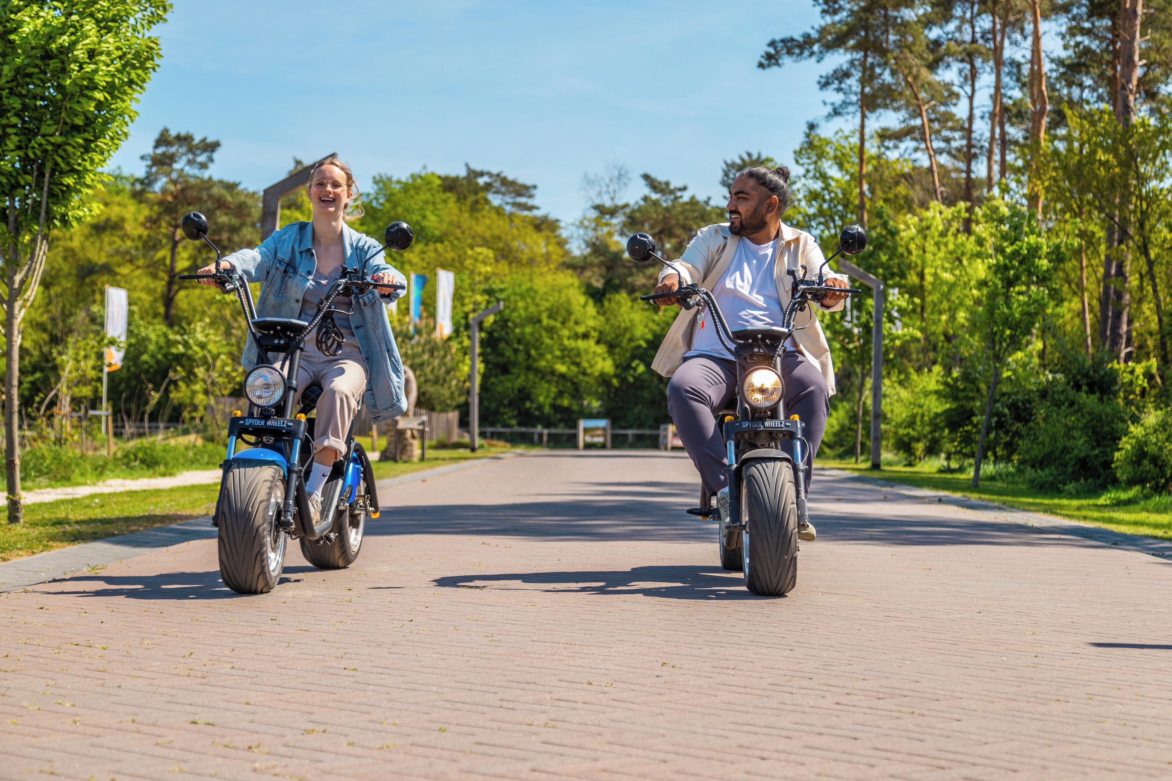 Twee personen fietsen op een verhard pad, omgeven door groen.