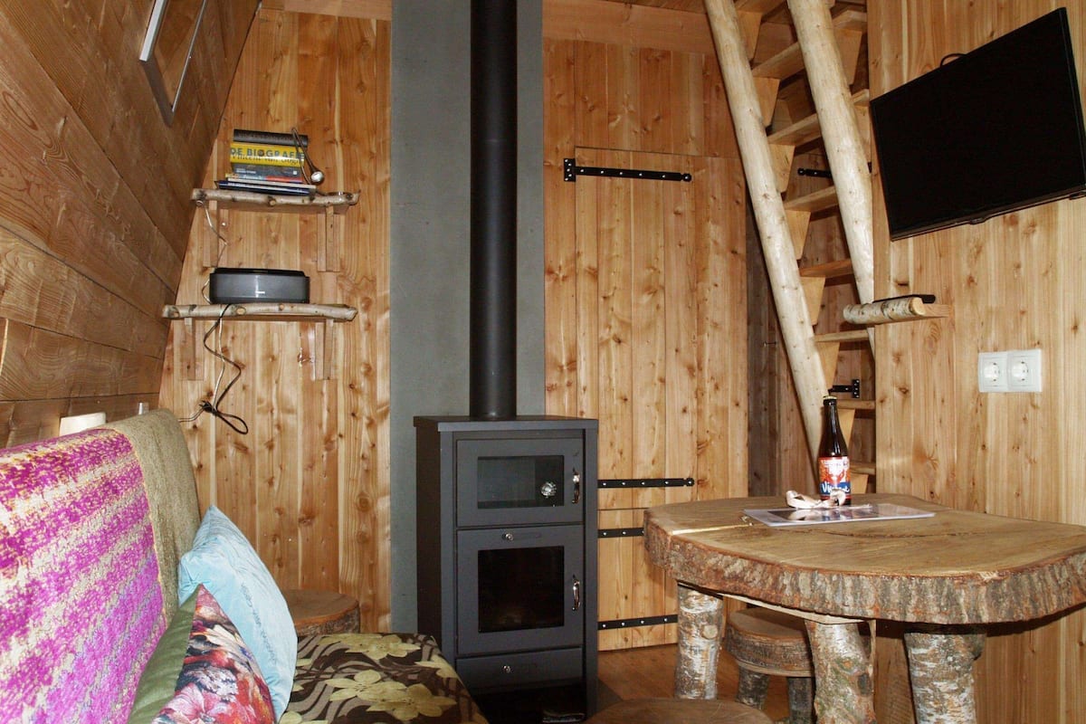 L’intérieur chaleureux d’un chalet avec un poêle à bois, une table en bois et un téléviseur fixé au mur.