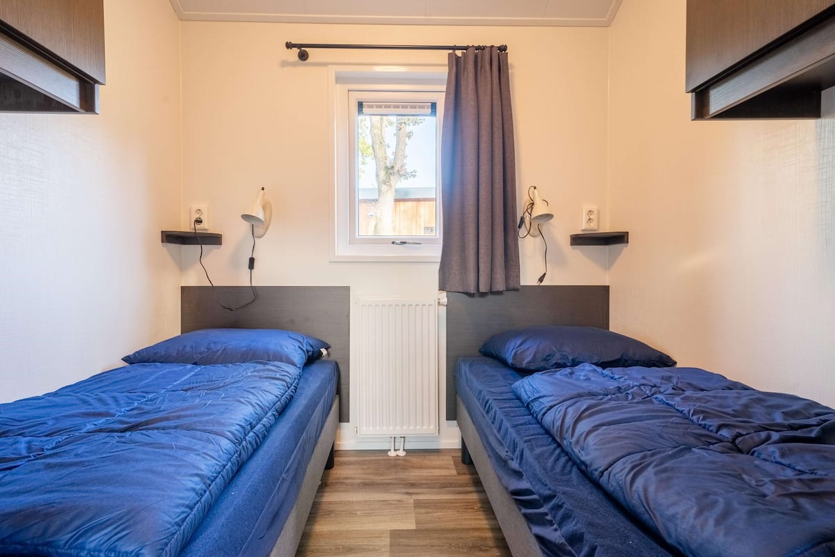 Une chambre avec deux lits, une fenêtre donnant sur un beau paysage, un radiateur et des étagères fixées au mur.