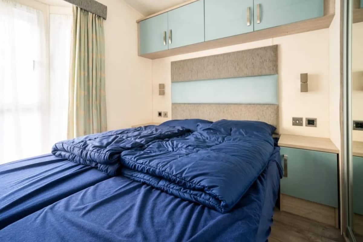 Un lit avec une literie bleue, une commode bleu clair et un mur gris à la texture particulière.