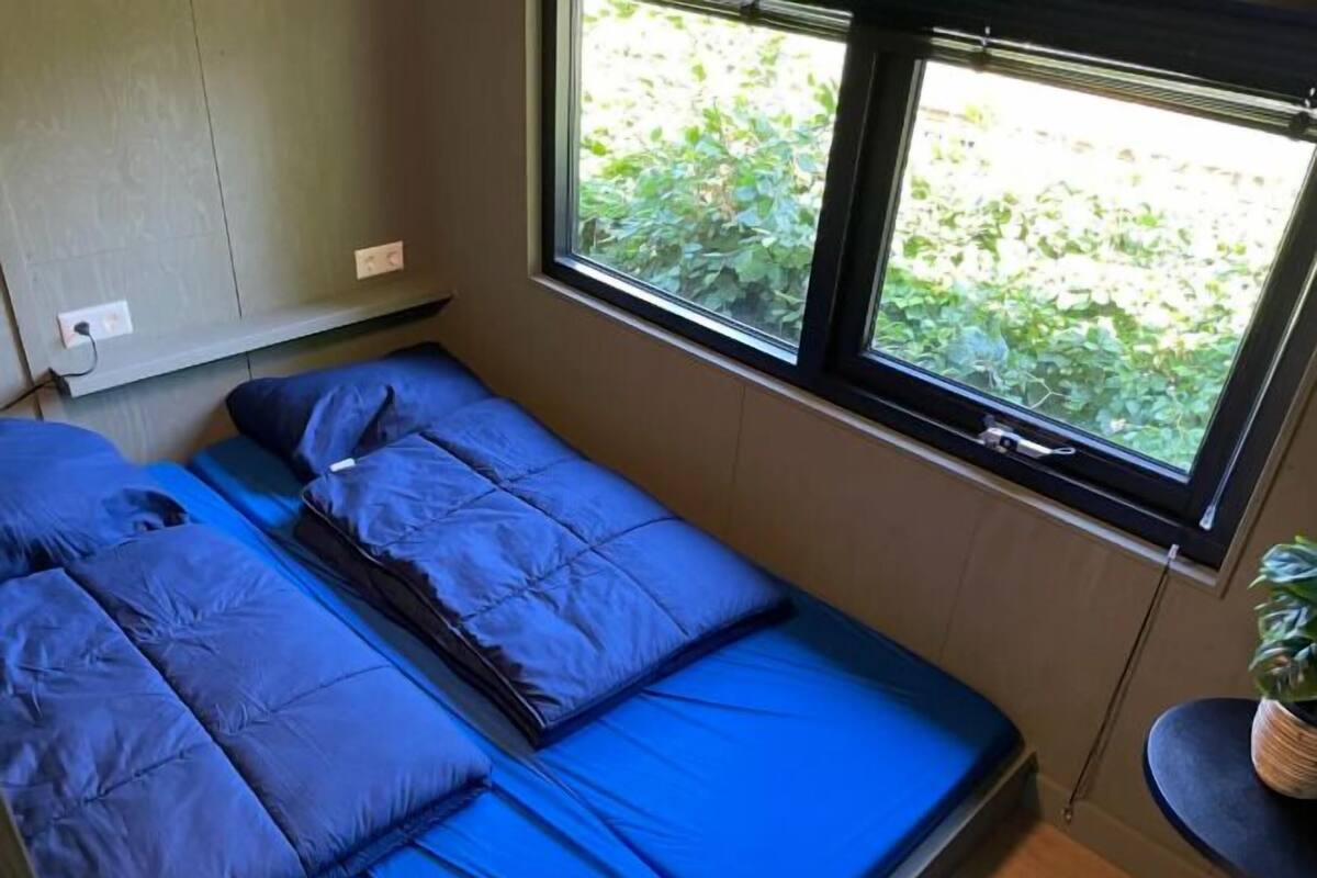 Un lit simple avec une literie bleue, dans une pièce dotée d’une fenêtre.