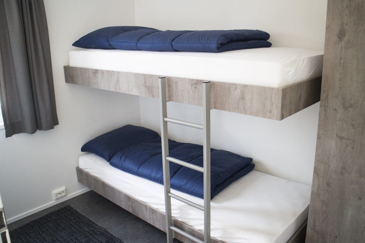 Un lit superposé avec une échelle, du linge de lit blanc et des oreillers bleus.