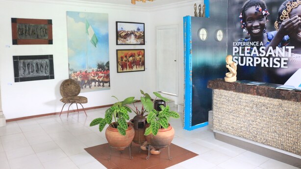 A reception area with a wooden ceiling, framed artwork on the walls, a reception desk, and potted plants. - NatureMark Gallery and Guest House (Uyo)