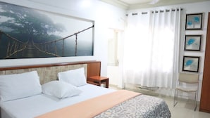 A hotel room with a bed, a nightstand, a chair, a window with curtains, and a wall-mounted picture. - NatureMark Gallery and Guest House (Uyo)