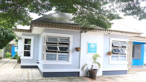 A building with a tiled roof, white walls, and multiple windows. There are potted plants and a sign on the wall. - NatureMark Gallery and Guest House (Uyo)