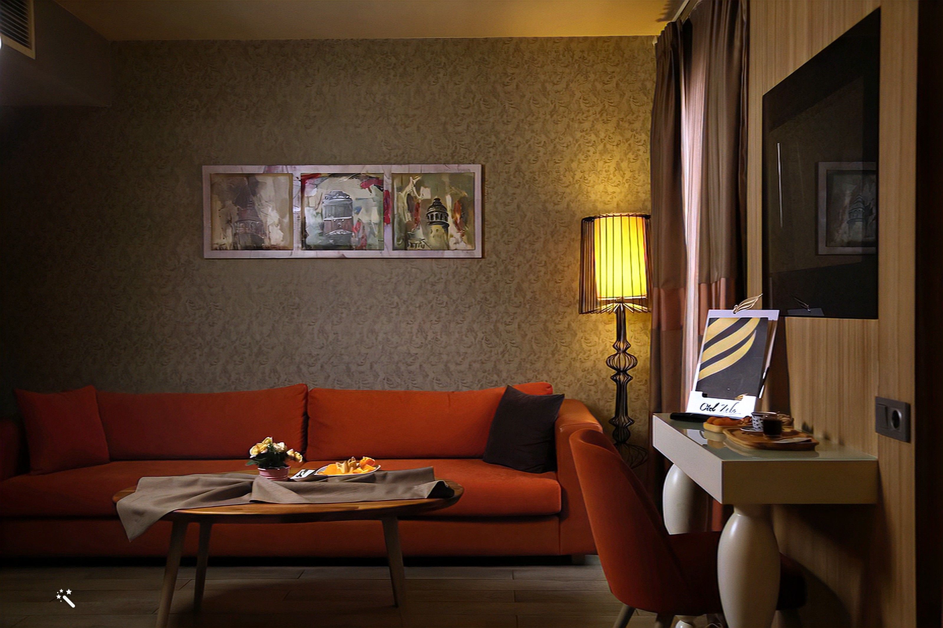 A hotel room with a red sofa, a small table with a lamp, and a desk with a computer and a chair.
