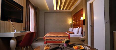 A hotel room with a bed, a desk, a chair, and a dining table with breakfast items.
