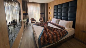 A modern hotel room with a large bed, a desk, two chairs, and a large window with curtains. - Hotel Zade (Erzurum)