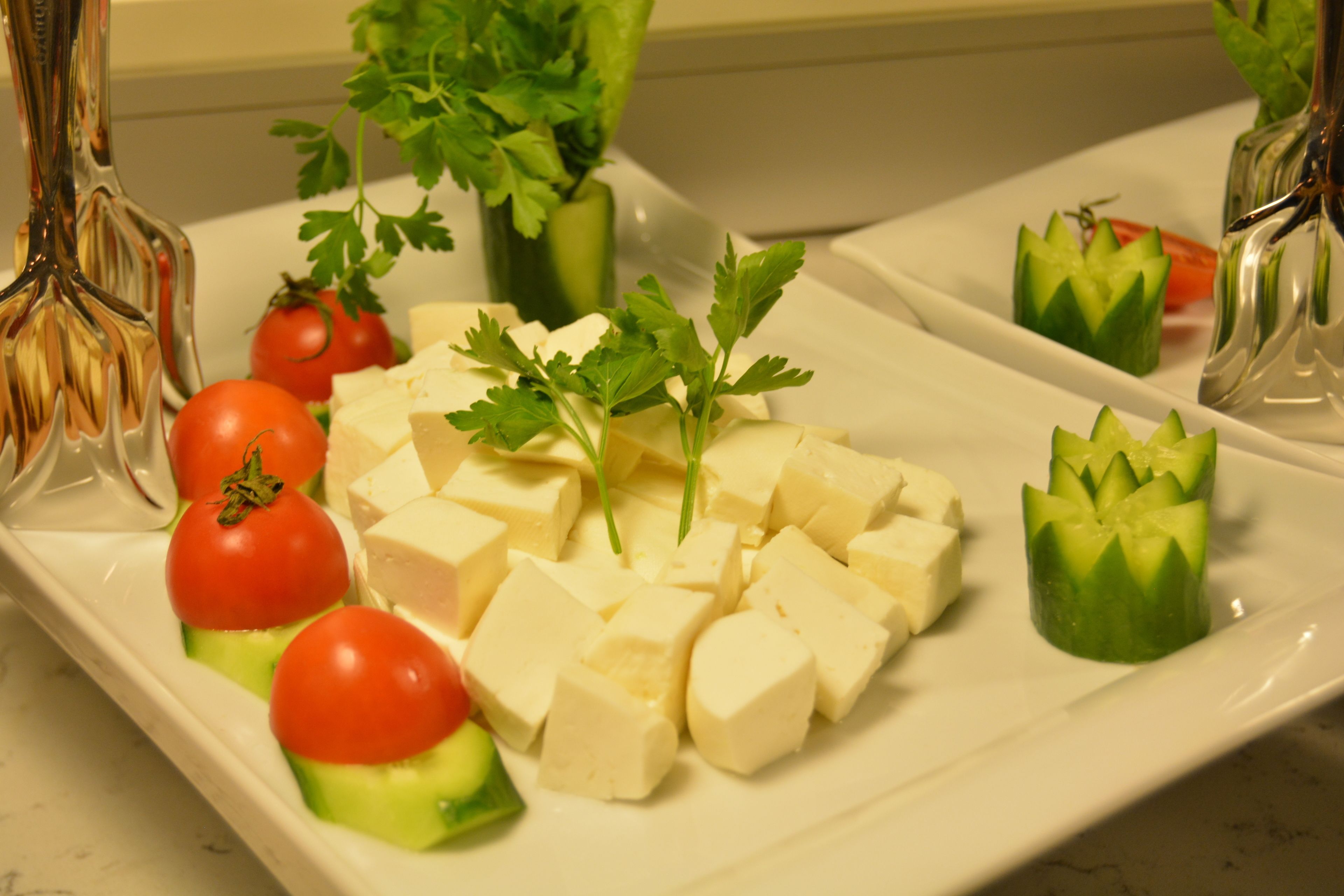 A white rectangular plate with cubed cheese, cherry tomatoes, cucumber slices, and parsley garnish.