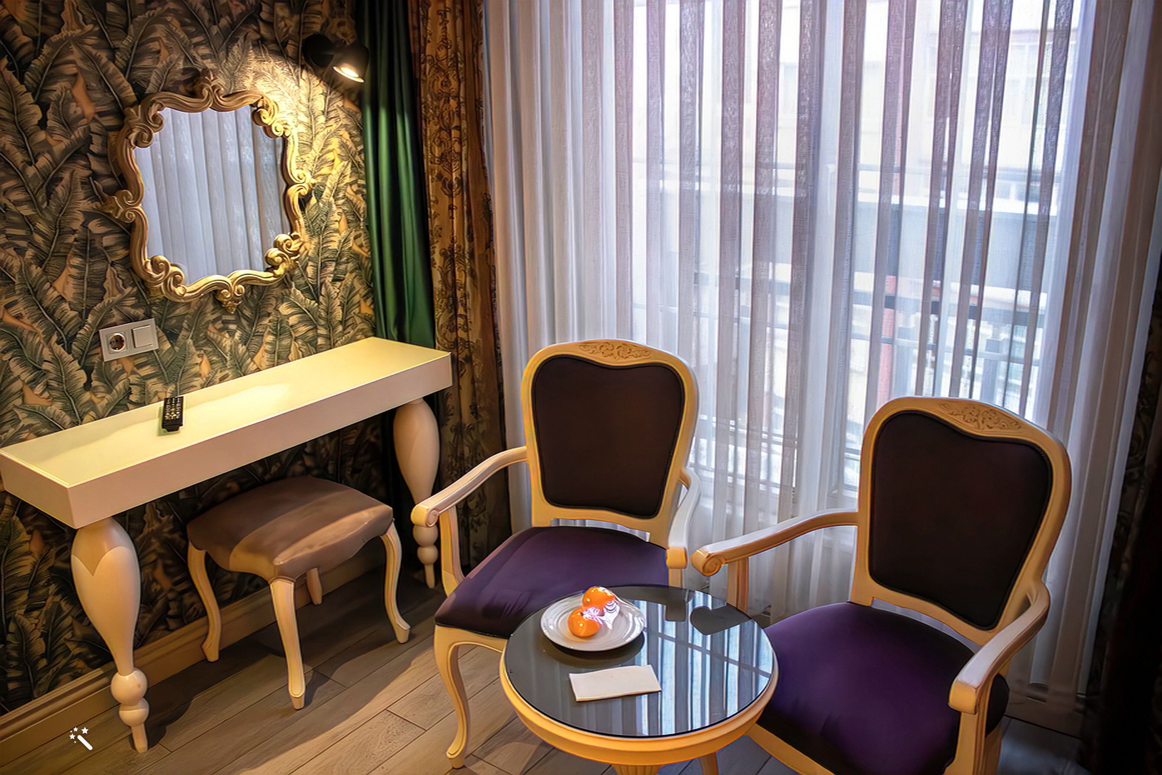 A room with a vanity, two chairs, a round table, and a mirror on the wall.
