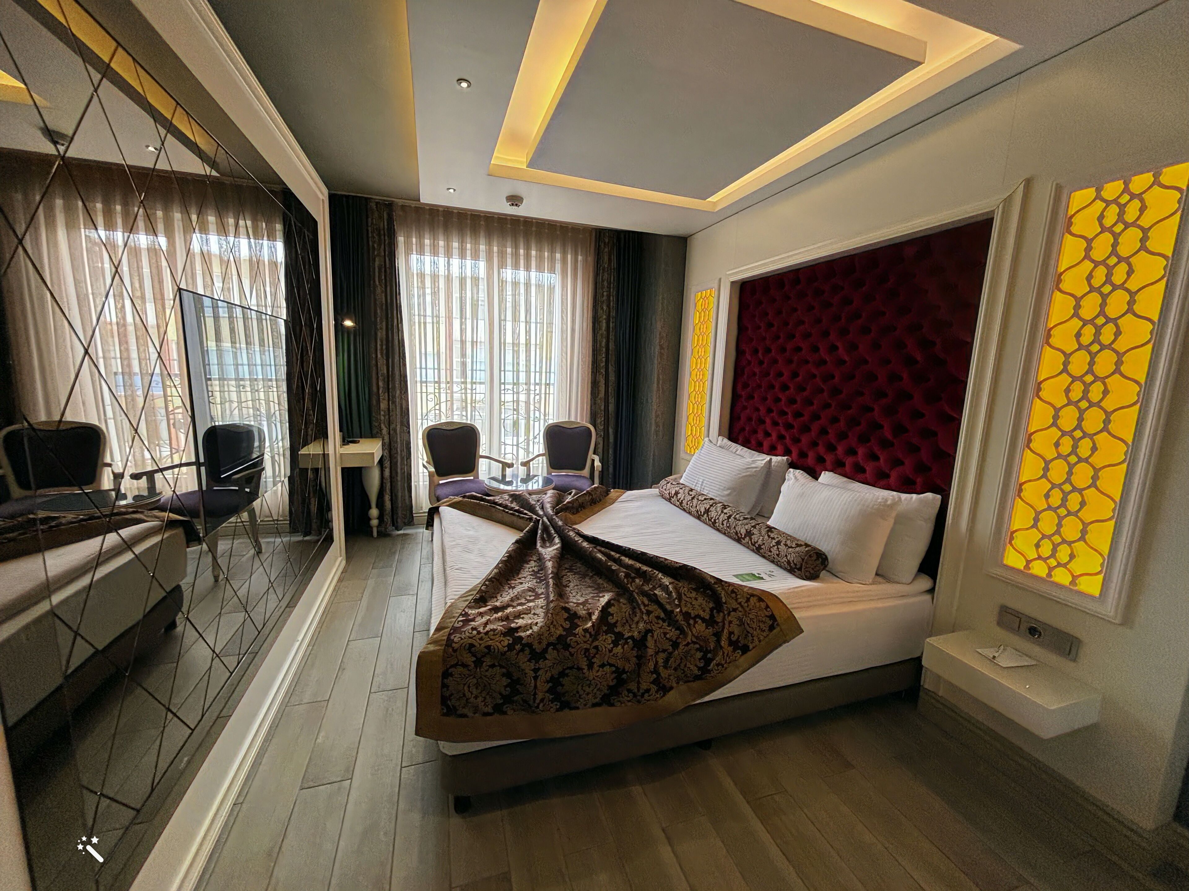 A hotel room with a large bed, two armchairs, a small table, and a desk with a chair.