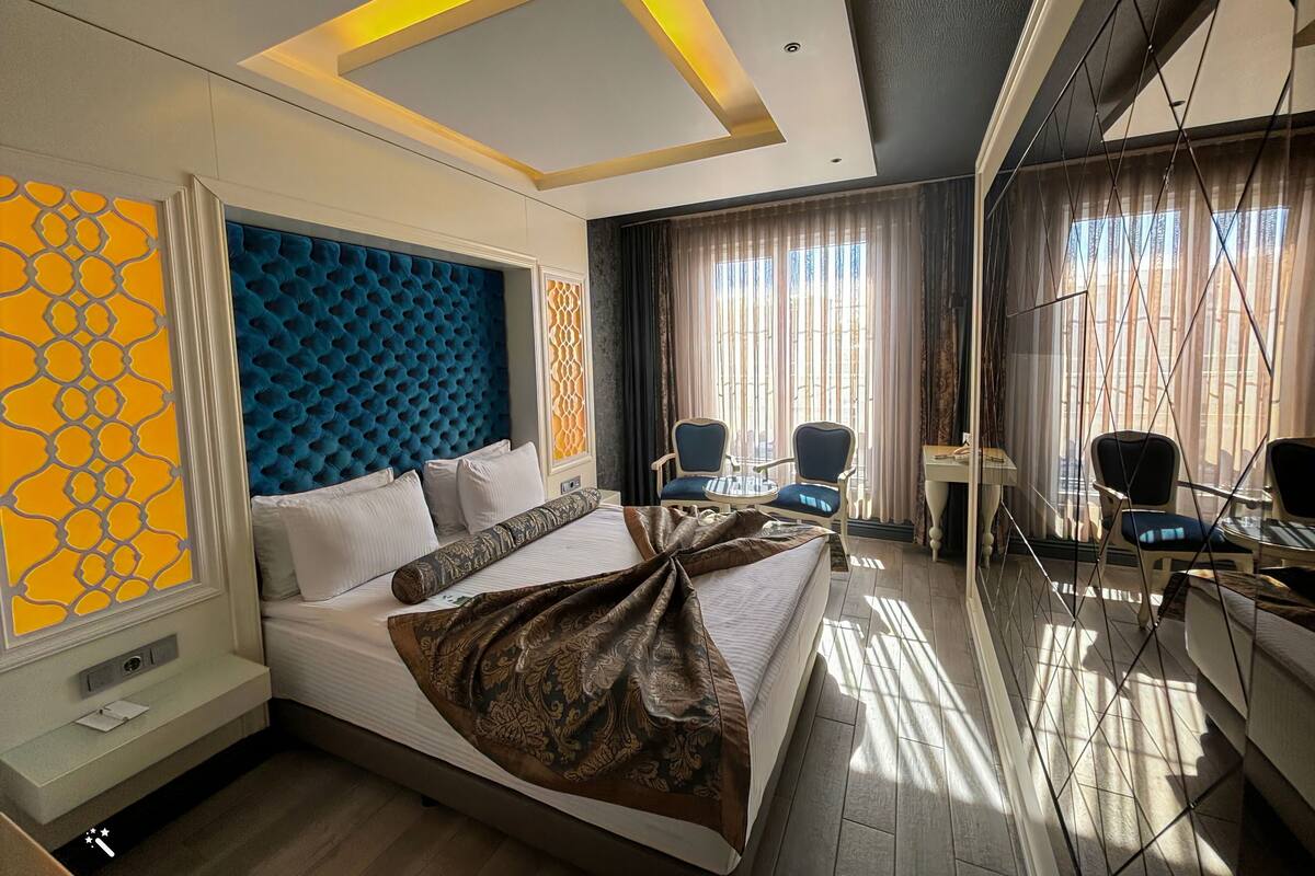 A hotel room with a large bed, a desk with two chairs, a window with curtains, and a decorative headboard.
