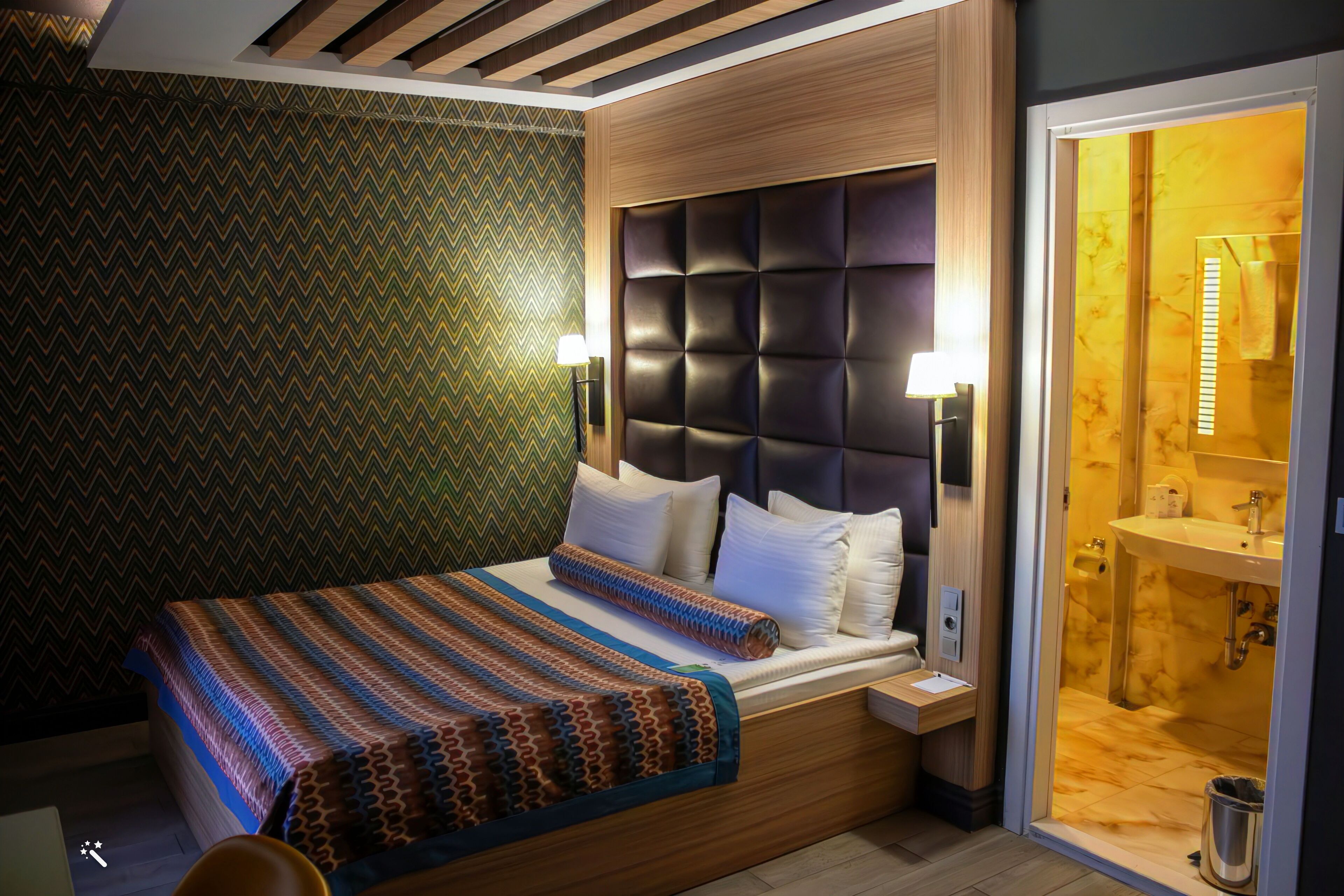 A modern hotel room with a large bed, a wooden headboard, and a bathroom with a marble sink.