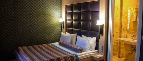 A modern hotel room with a large bed, a wooden headboard, and a bathroom with a marble sink.