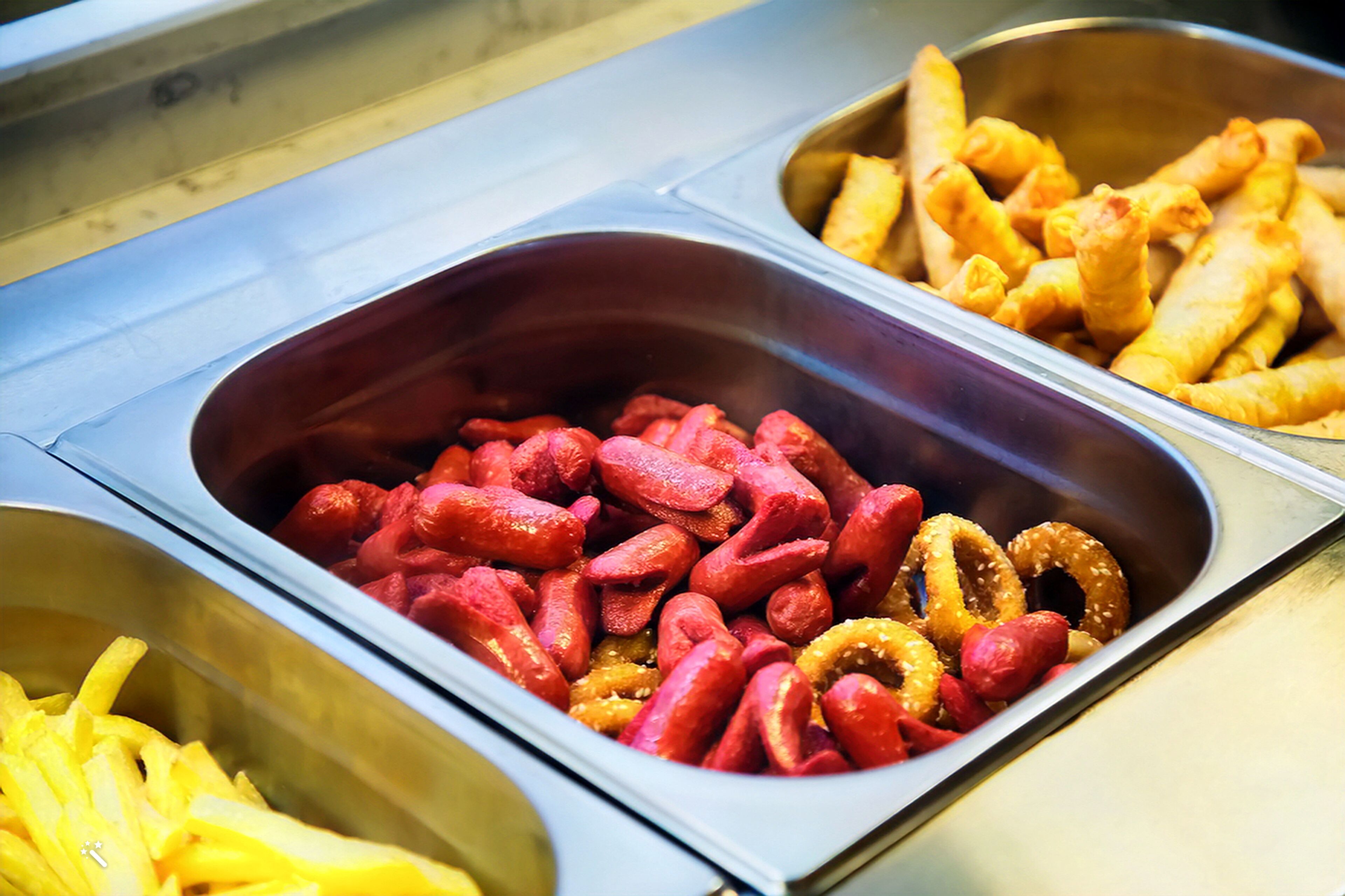 Buffet com diversos alimentos, incluindo salsichas, anéis de cebola e batatas fritas.