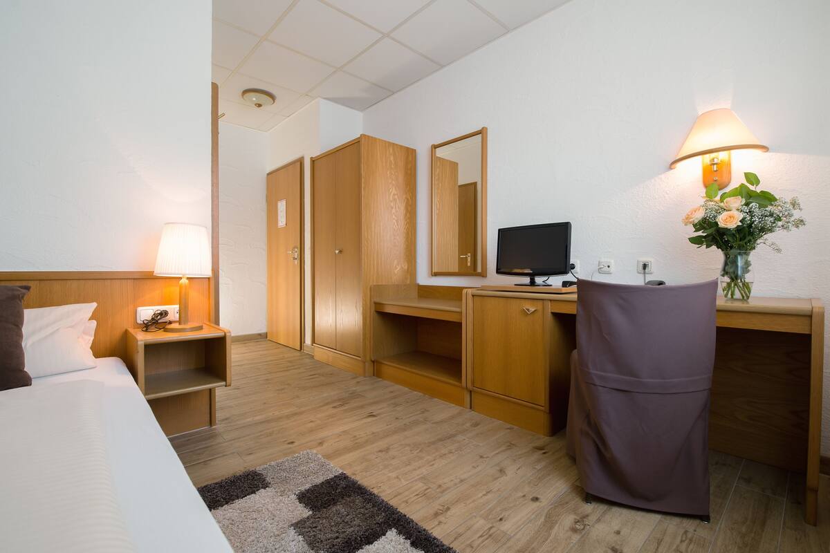 Ein Hotelzimmer mit Bett, Schreibtisch, Stuhl, Fernseher, Lampe, Spiegel und einer kleinen Schreibtischlampe.