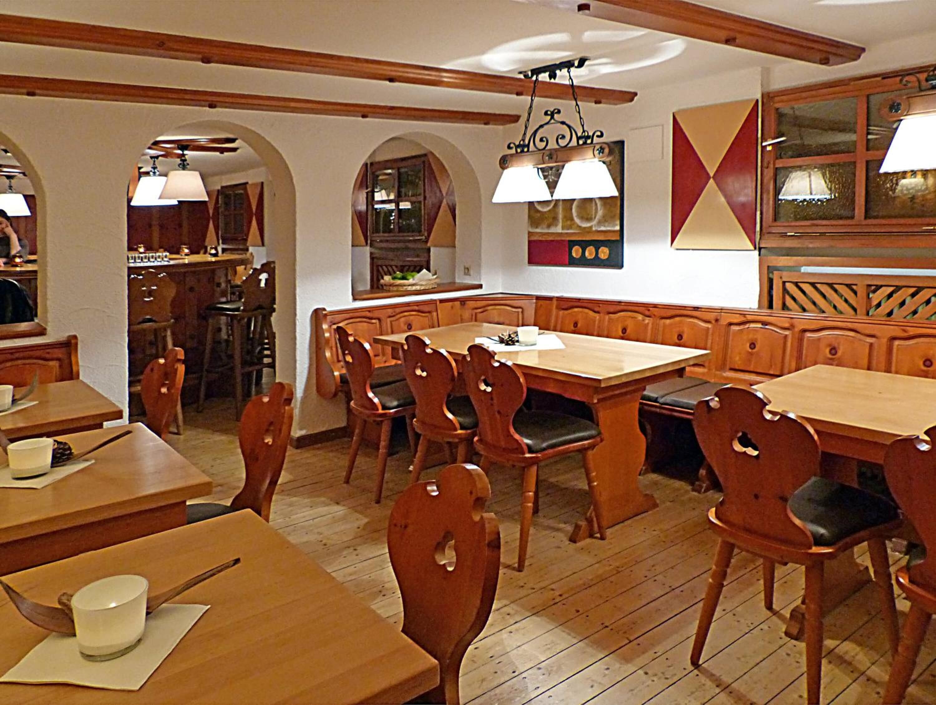 A restaurant with wooden tables and chairs, a bar area, and a kitchen visible through an archway.