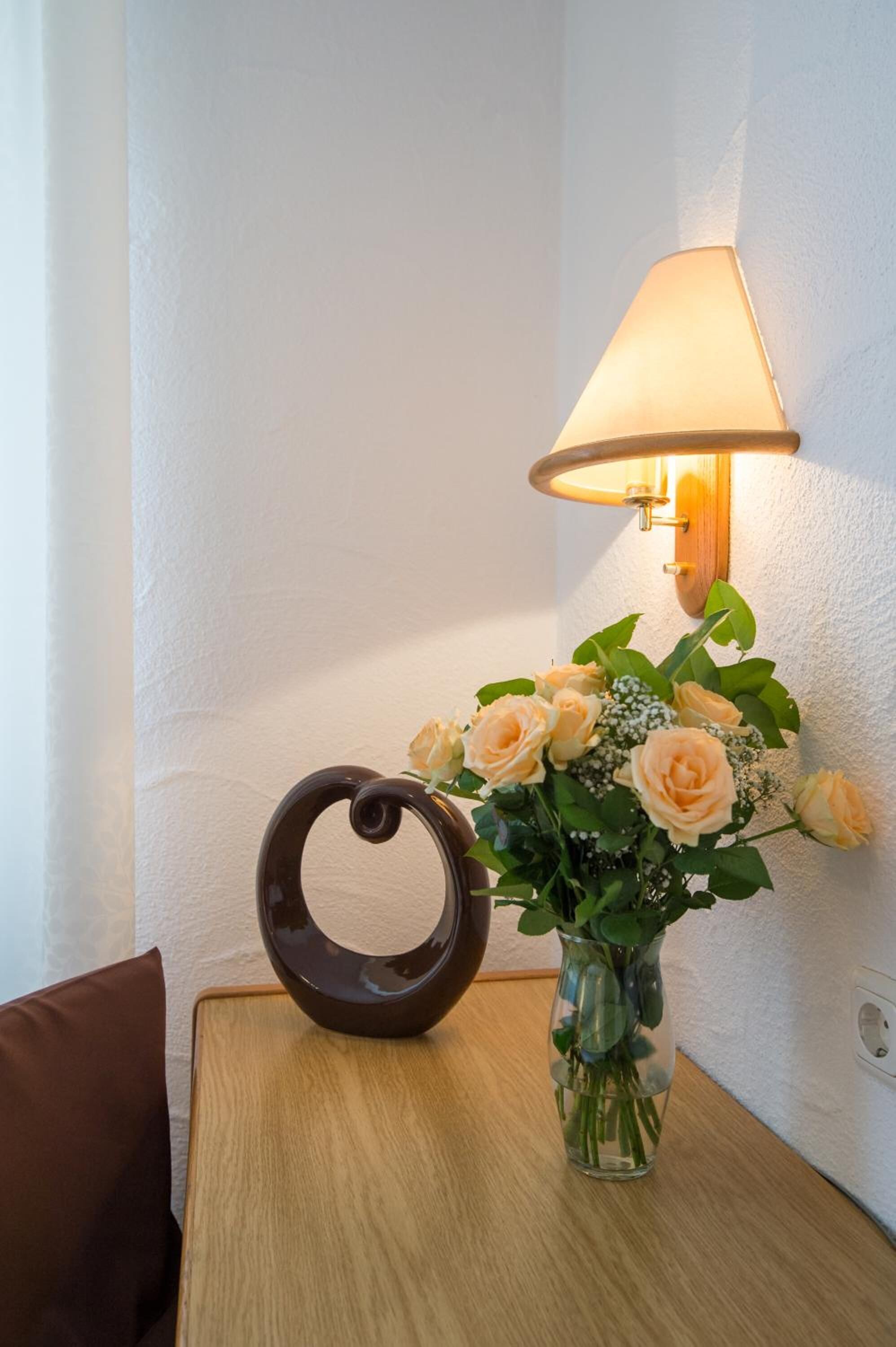 Una mesa con un jarrón de flores y una lámpara de pared.