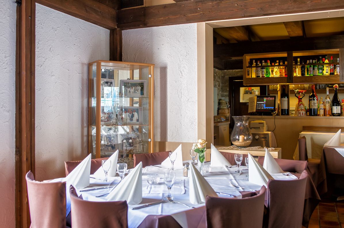 Restaurante com mesas preparadas para refeições, área de bar com garrafas e um expositor com diversos itens.