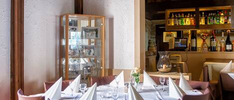 Restaurante com mesas preparadas para refeições, área de bar com garrafas e um expositor com diversos itens.