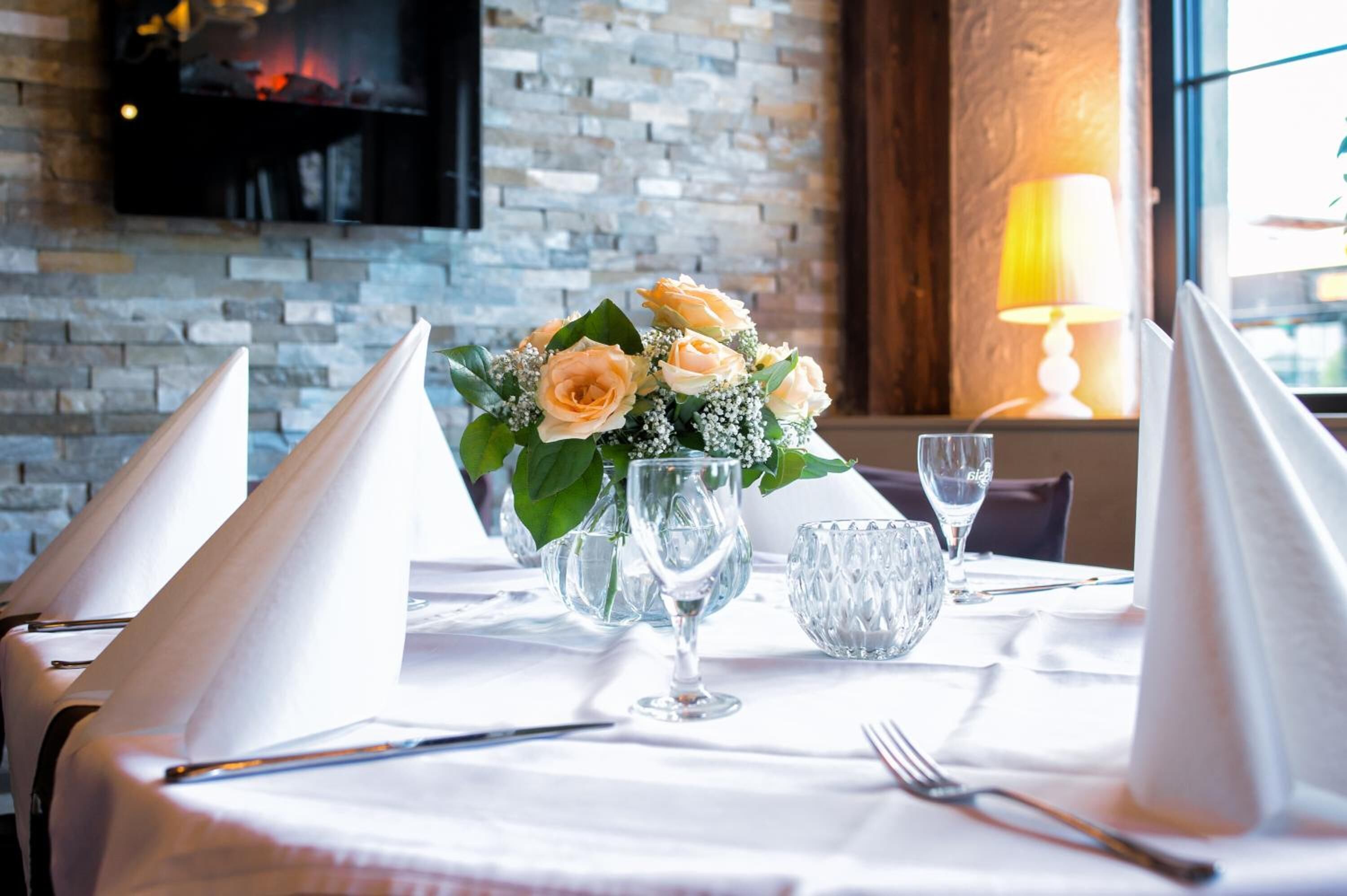 A dining table set with white napkins, a vase of flowers, and clear glassware.