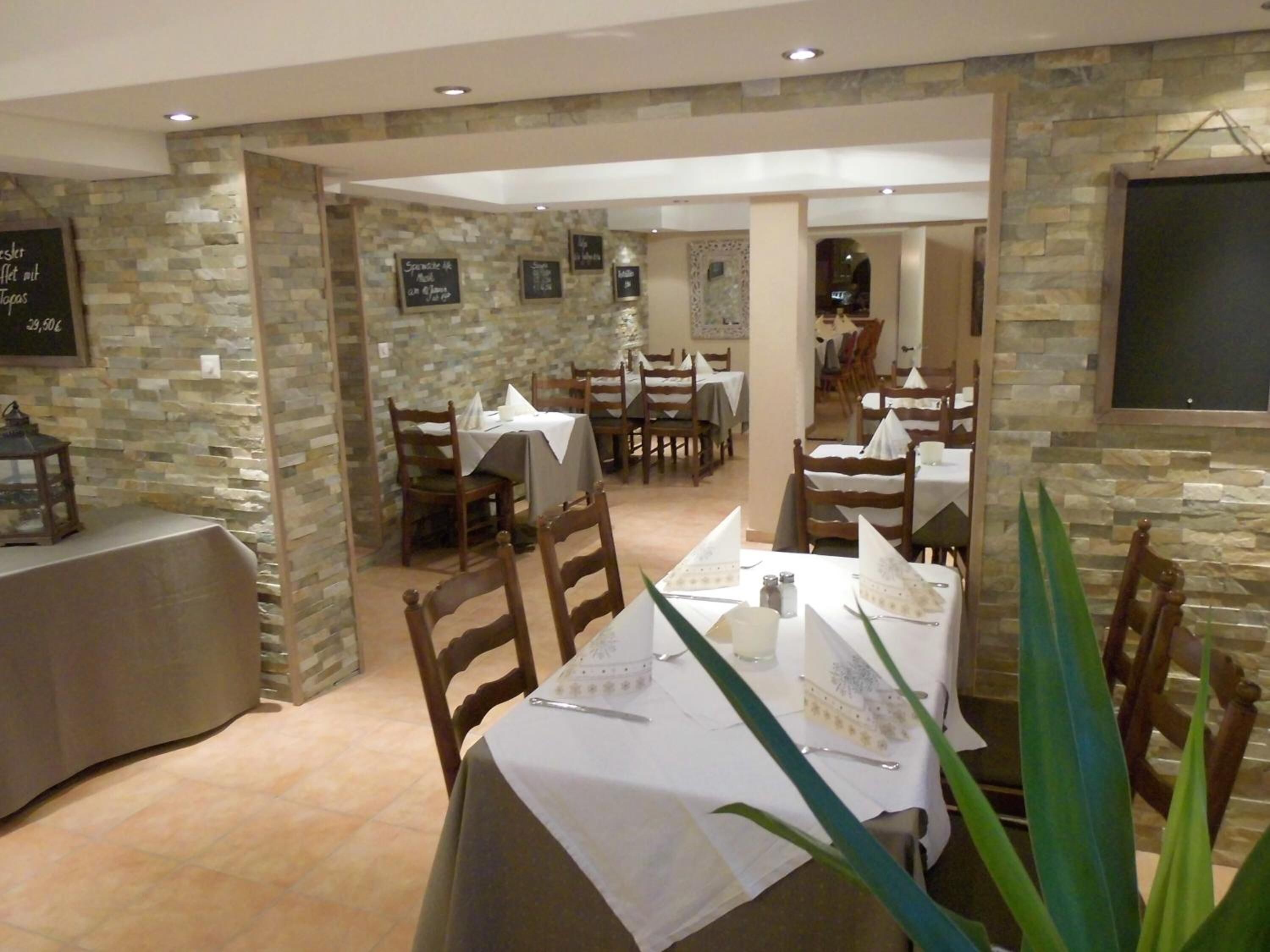 Restaurante com paredes de pedra, mesas e cadeiras de madeira.