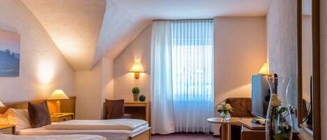 Una habitación de hotel con dos camas, un escritorio con computadora, un televisor y un florero con flores.