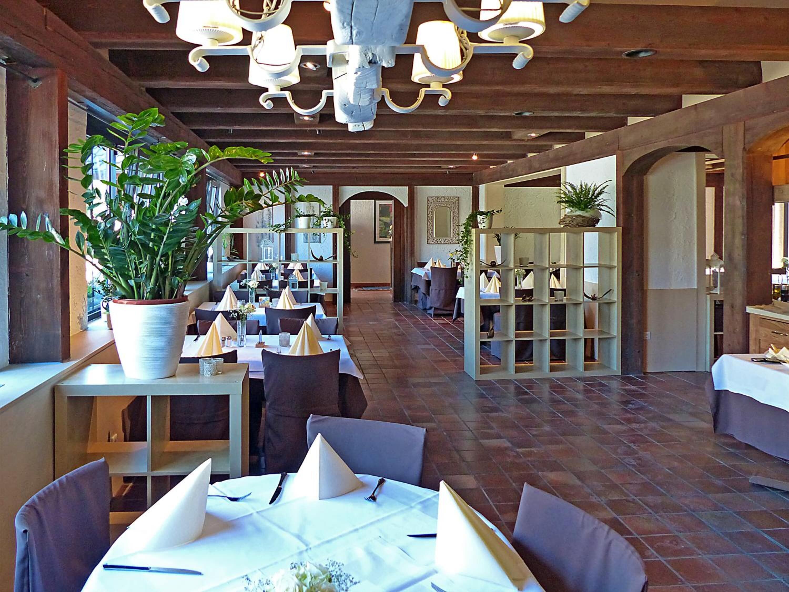 A restaurant with wooden beams, potted plants, and tables set for dining.