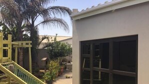 Patio trasero residencial con zona de juegos, que incluye un tobogán y una estructura para escalar, rodeado de macetas con plantas y una palmera.