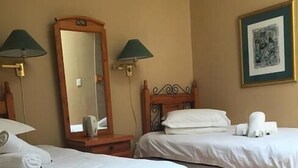 Habitación de hotel con dos camas individuales, un espejo grande, dos lámparas de pared y un cuadro enmarcado.