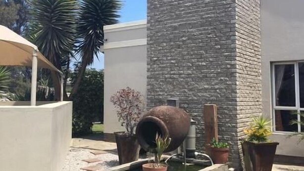 Un edificio moderno con fachada de piedra, una fuente de agua y plantas en macetas.