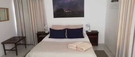 A bedroom with a bed, two bedside tables, a nightstand, a bench, a painting, and curtains.