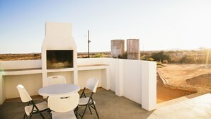Un patio al aire libre con una parrilla, sillas blancas y una mesa.