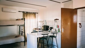 Cocina compacta con una isla central, una litera y una puerta que da a otra habitación.