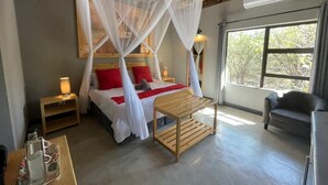 A bedroom with a bed under a canopy, bedside lamps, a wooden table, and a view of trees through a window.