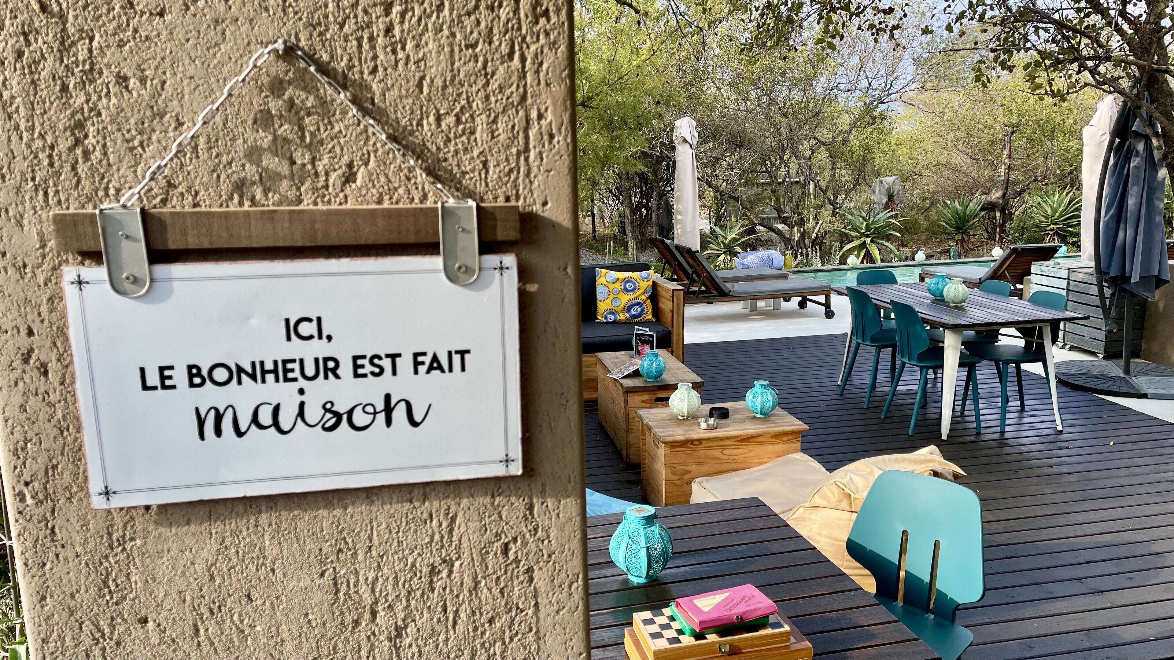 A sign with French text, a wooden deck with outdoor furniture, and a pool area.