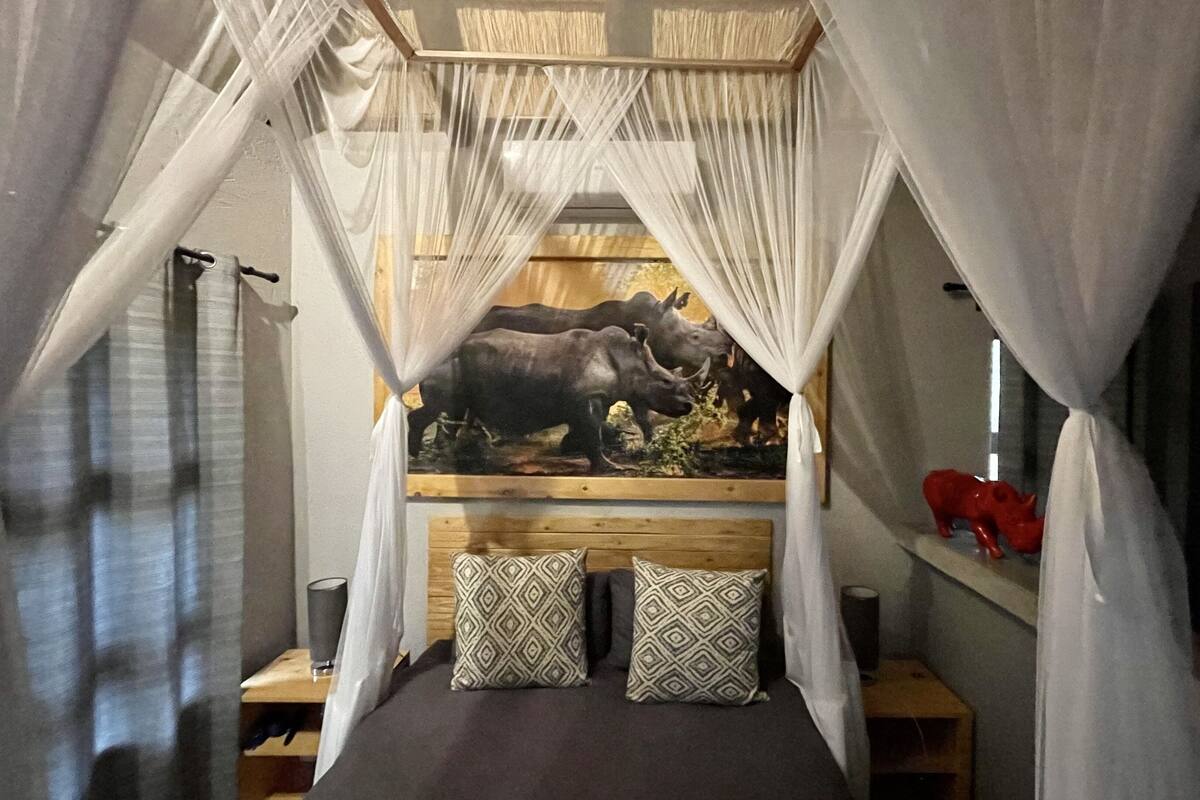 A room with a canopy bed, a mural of rhinos, and a small shelf with a red pig figurine.