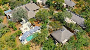 An aerial view of a residential area with multiple houses, a swimming pool, and surrounding greenery.
