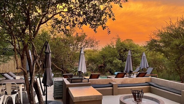 An outdoor seating area with lounge chairs and umbrellas, surrounded by trees and a sunset view.